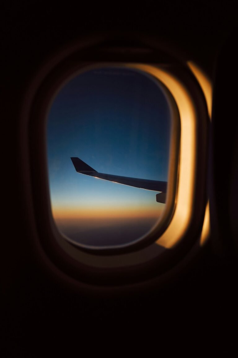 Airplane window view of a wing against a navy sky and gold sunset horizon