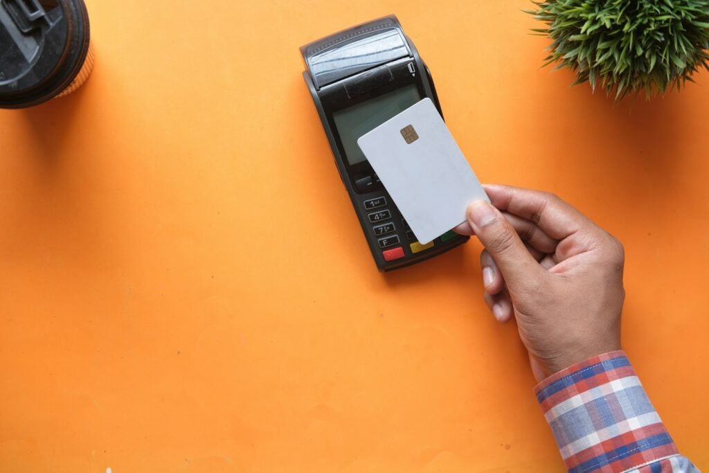 Hand holding a blank white credit card above a card payment terminal on an orange background